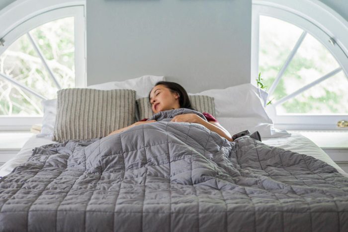 Woman Sleeps Under Grey Weighted Blanket on White Sheets in a Bright Bedroom