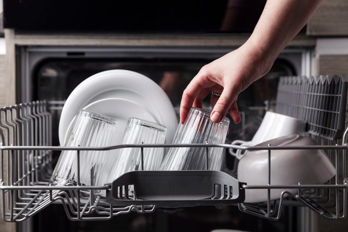 Close-up of Female Emptying Out an Open dishwasher with clean dishes inside