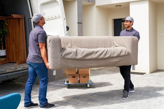 Male Delivery Coworkers Unloading Sofa From Moving Van Near House