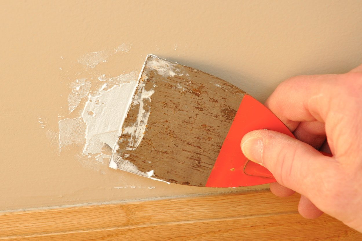 Putty Knife With Spackling Paste against a wall and wood molding