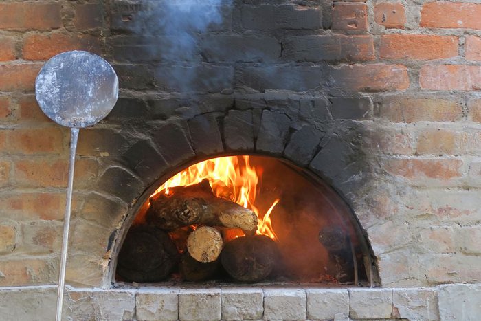 Traditional Brick Outdoor Pizza Oven, with Wood Burning Logs, open flames and a long handled, metal pizza paddle shovel