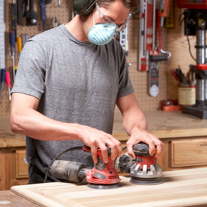 A Man Sanding Wood With Both Hands on Two Sanders