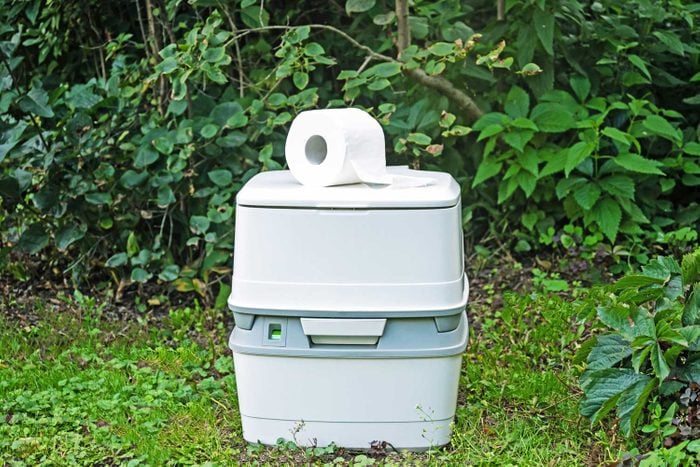 Chemical Portable Toilet with Toilet Paper Roll Resting on top in a green garden courtyard wooded area