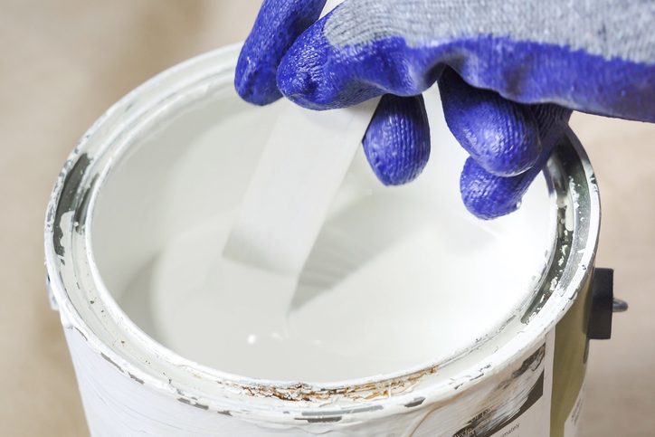 Close up of hand gloved painter mixing paint in metal paint can with wooden paint stick