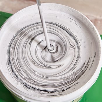 Painter uses an electric mixer to mix black and white paint to create gray color in a white paint mixing bucket