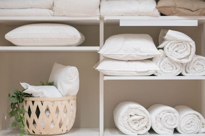 Various Household Items Such As Pillows And Quilts Standing In The White Cupboard of the laundry room