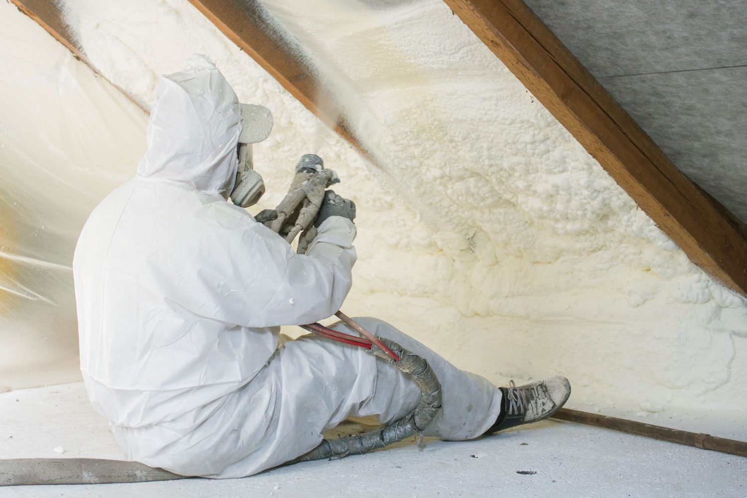 Technician uses spray gun for polyurethane foam to insulate home attic in a residential setting