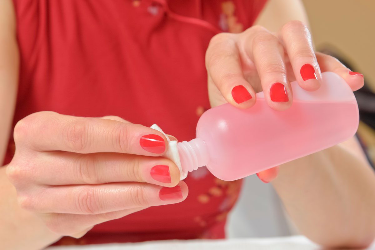 Young woman Dampens a Cotton Ball With Acetone Nail Polish Remover, Indicating Nail Polish Paint Removal, While Wearing Bright Red Nail Polish and a Bright Red Shirt
