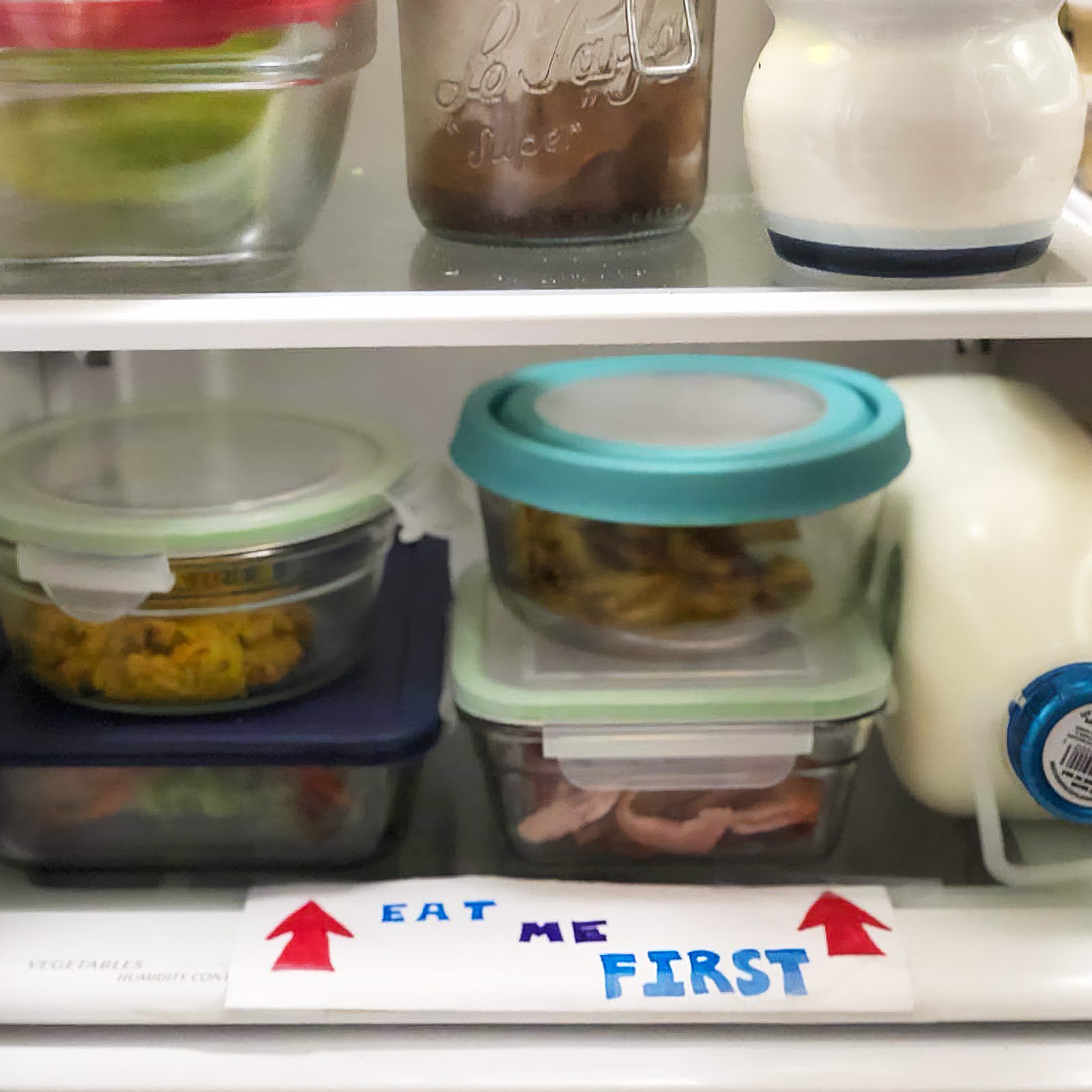 containers in fridge with "eat me first" label on bottom shelf