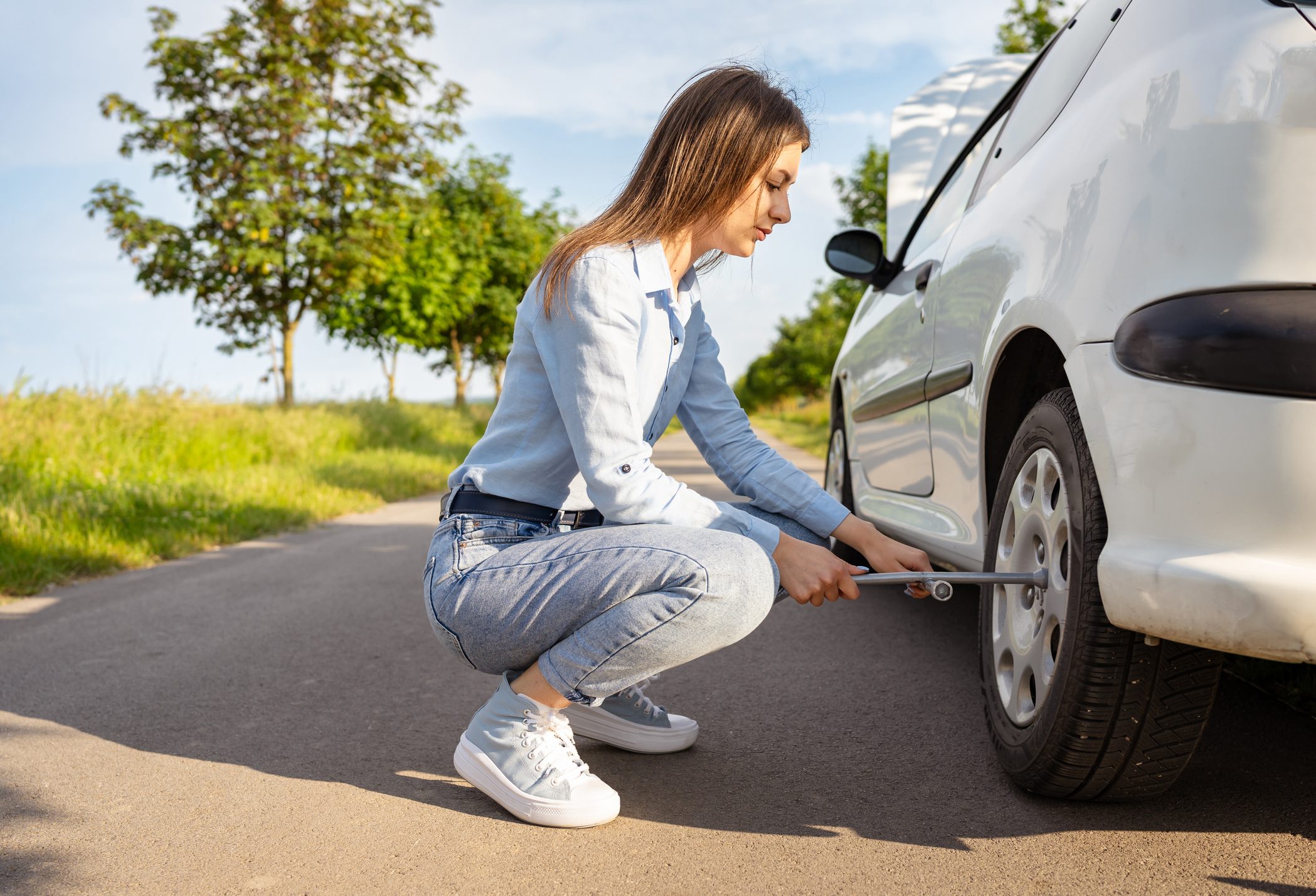Young woman independently uses a car tire jack on the road