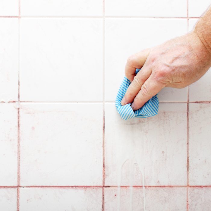 hand cleaning pink mold from bathroom shower grout