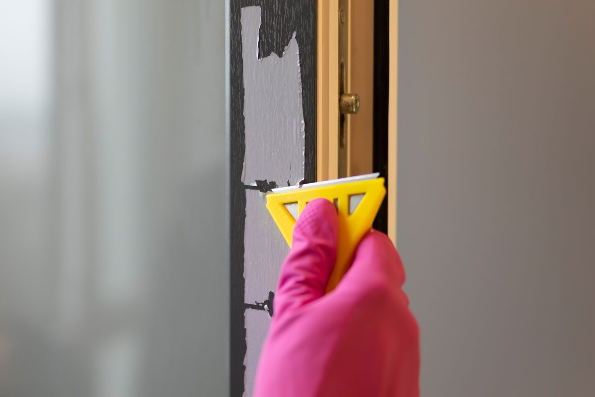 Removing Protective Tape From The Window Frame With Razor Blade Scraper and Pink Rubber Gloves