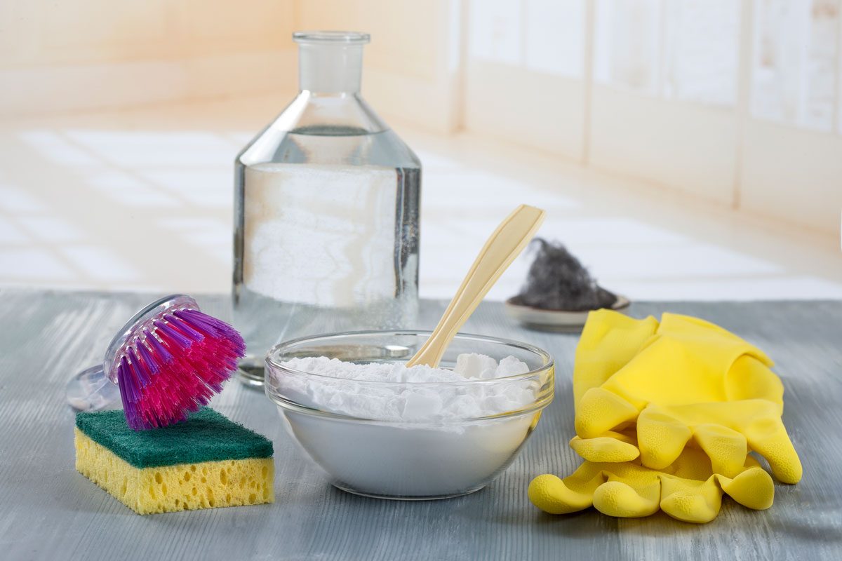 Home Made Natural, Chemical-Free Cleaners With Baking Soda and Vinegar Surrounded by Cleaning Gloves, Sponges, Scrubbers and a toothbrush