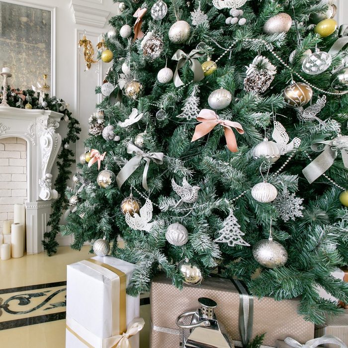 White fireplace decorated with candles and fir branches. Decorated Christmas tree. Classic apartments, morning in hotel