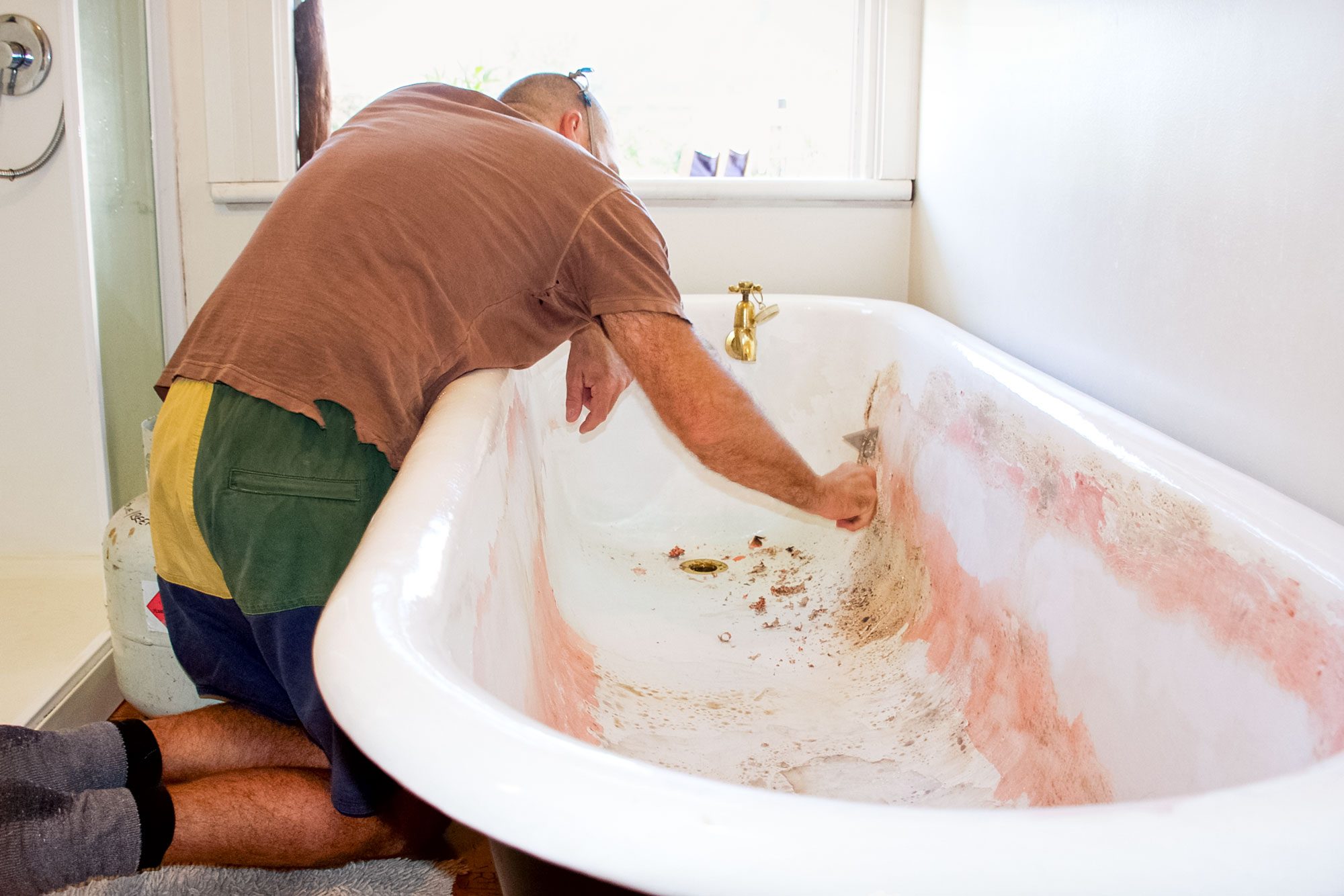 A Man Strips Away The Old Paint Of A Cast Iron Bathtub