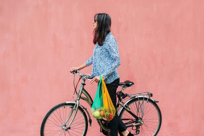 sustainable woman with a bike and reusable grocery bags filled with produce on a light pink wall outside