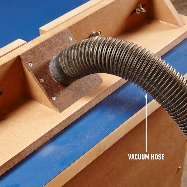 A vacuum hose is attached to a wooden router table for double dust collection.