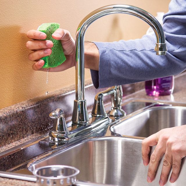 Dribbling water around the sink rim and faucet base with a sponge