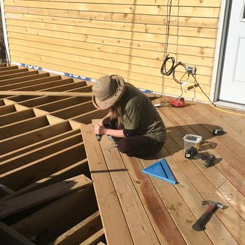 A woman is working on a wooden deck in front of a house.