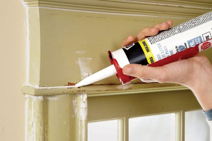 A person using caulk to fill gaps and cracks in a window