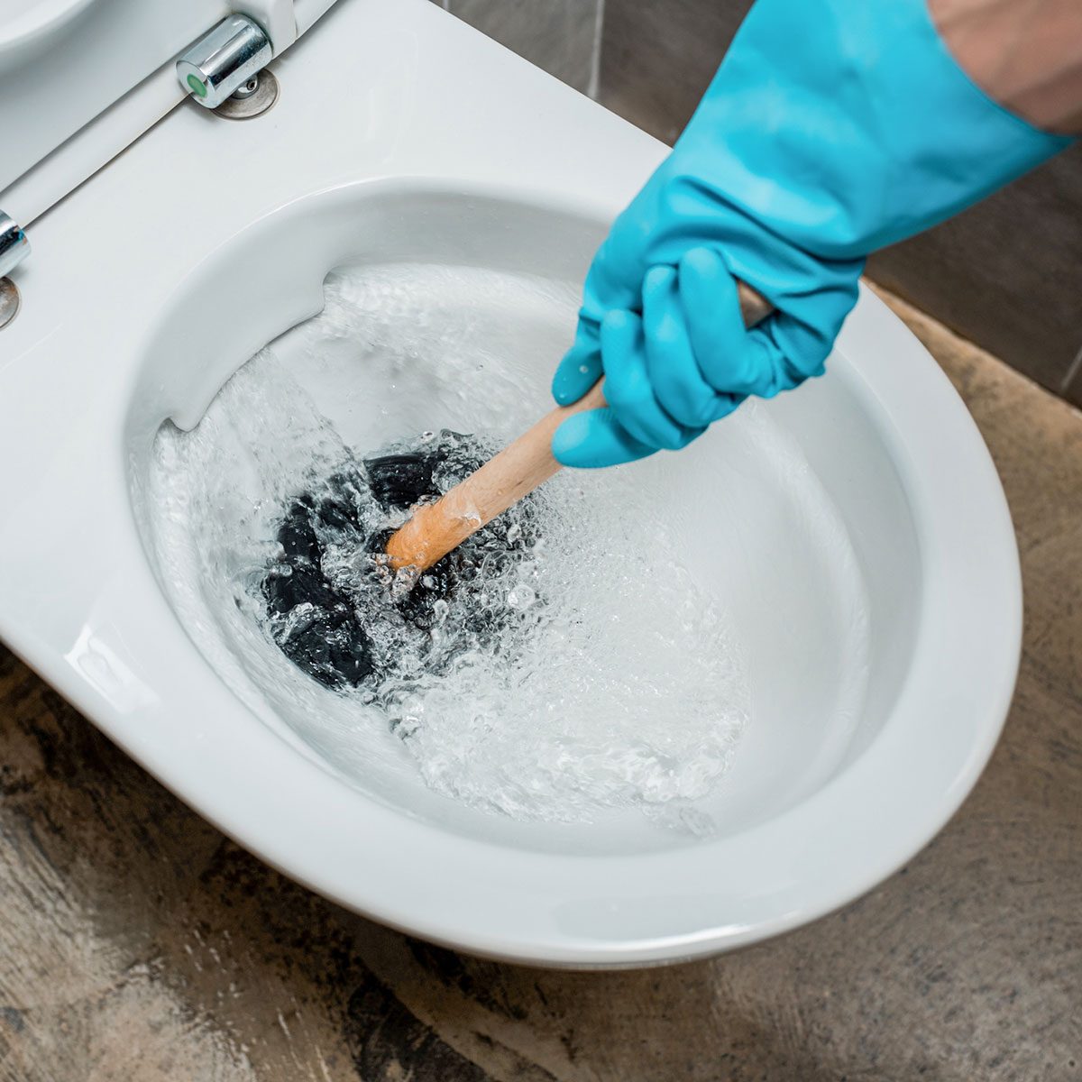  plumber using plunger in toilet bowl during flushing in modern restroom with grey tile