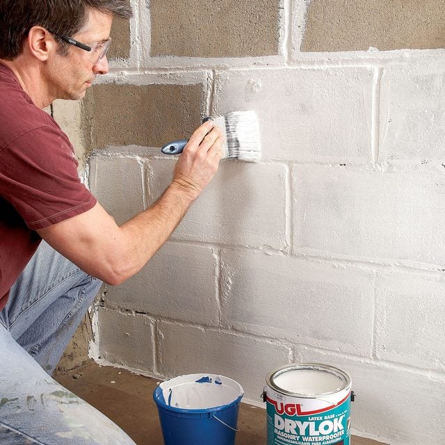 a person applying waterproofing paint on basement wall