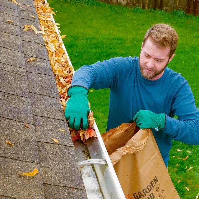 a person cleaning a clogged rain gutter full of dried leaves