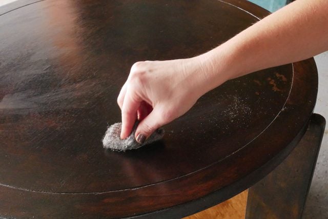 A person using steel wool sanding on a wooden table