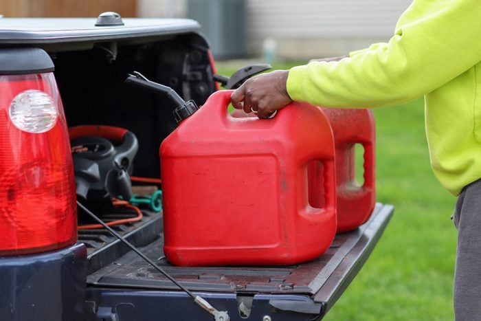 An African-American man holding two red plastic gas tank in a truck