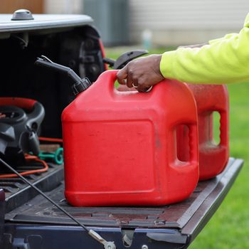 An African-American man holding two red plastic gas tank in a truck