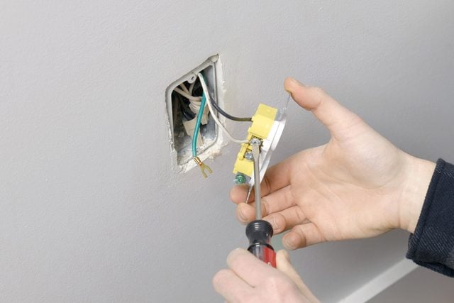 A person unfastening the screws in the electrical outlet