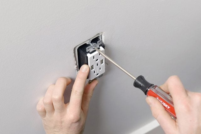 A person attaching the outlet wall plate cover with a screwdriver