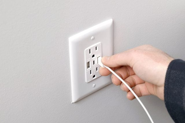 A hand plugging into a wall USB outlet