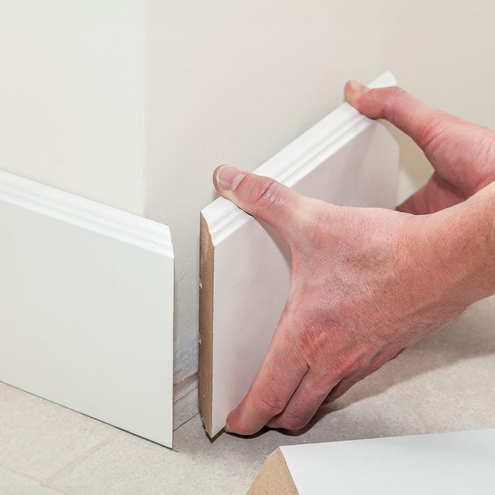 Man Putting New Baseboard Floor Trim Molding In House