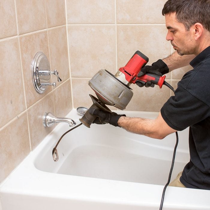 Plumber Unclogging A Tub Drain With An Electric Drain Snake