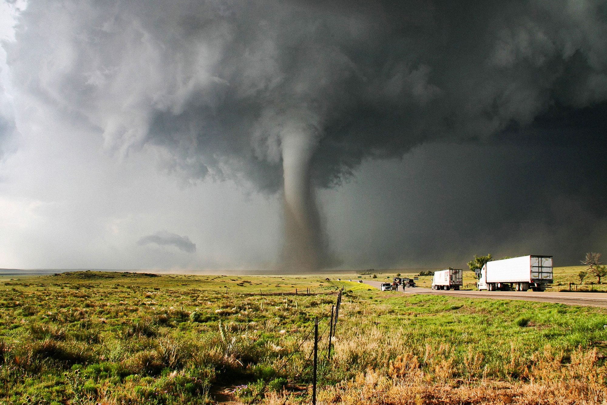 A Tornado With Green Area And Trucks On Road
