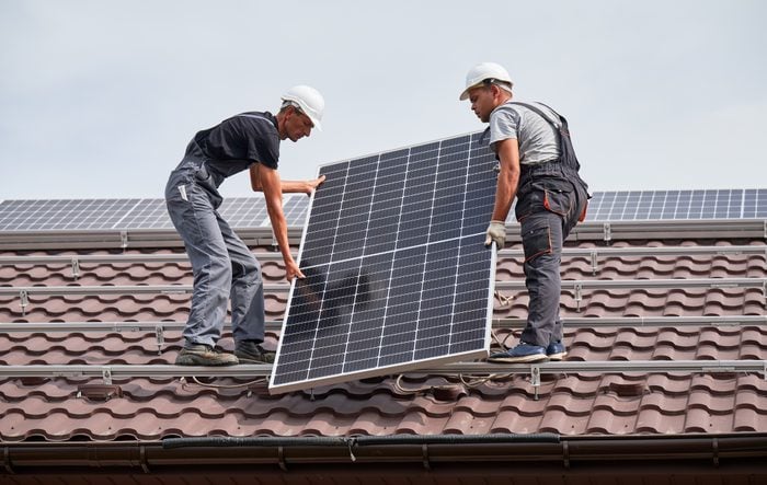 Man worker mounting solar panels on roof of house.
