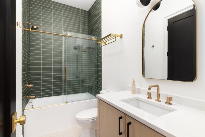 A bathroom with gold accents and a shower with green subway tiles.