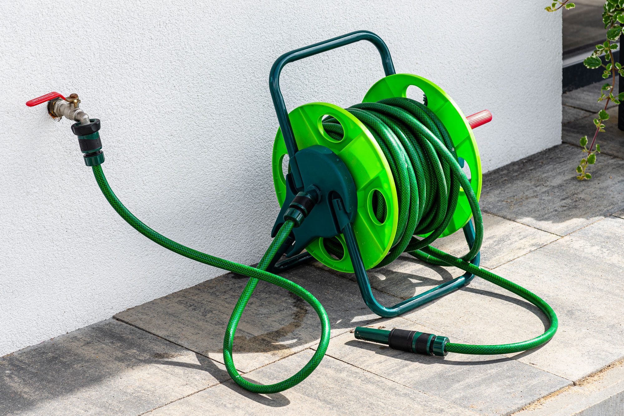 A Garden Hose Connected To A Faucet Protruding From A Building Against A White Facade