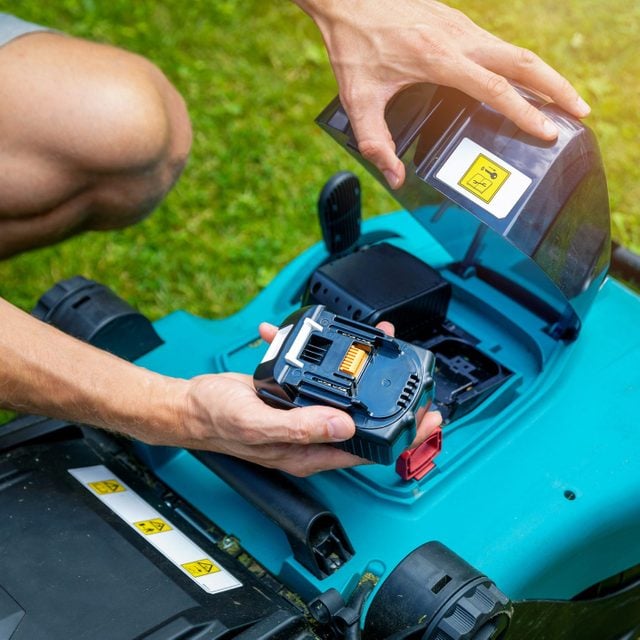 man putting battery into electric cordless lawn mower