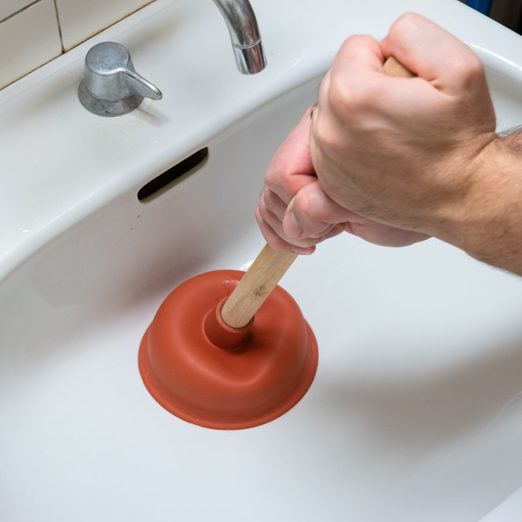 Caucasian male hand holding a plunger unclogging a bathroom sink