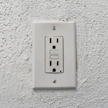 A close-up view of a weathered white wall socket with peeling paint, featuring a power outlet plug.