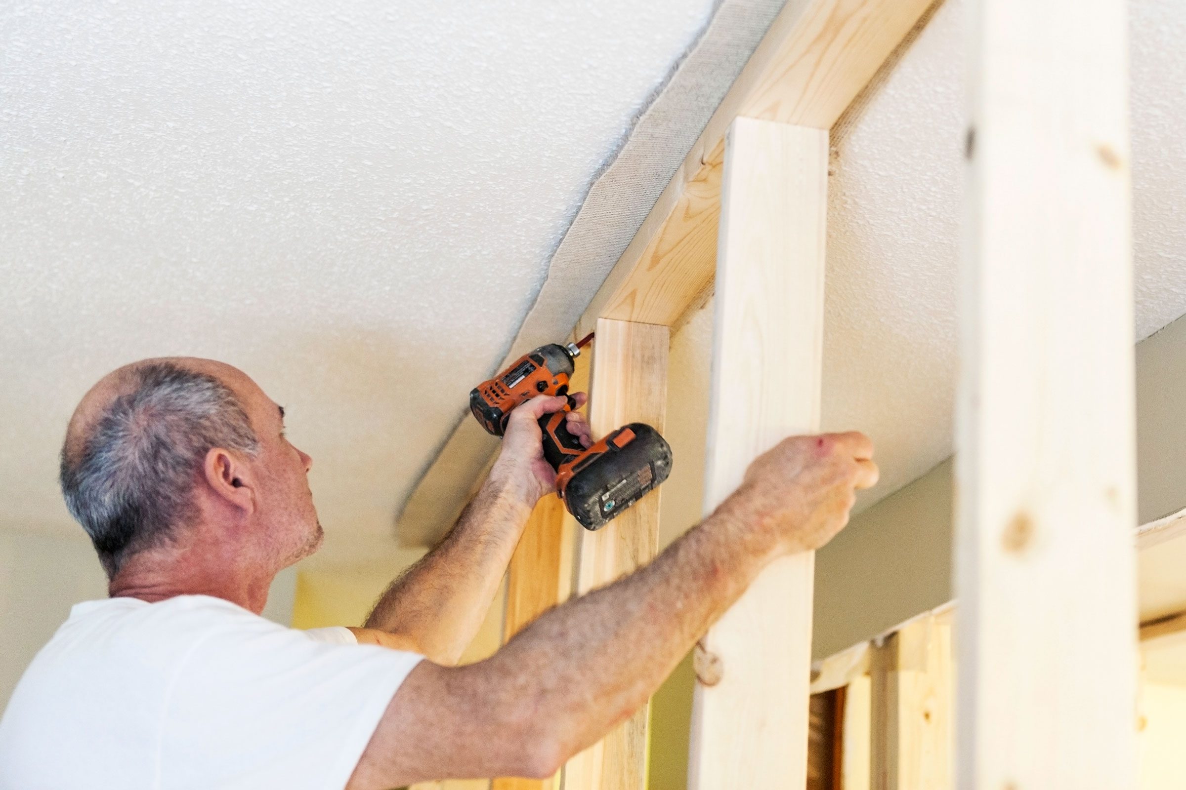 man drilling into a stud on a support wall during a home renovation